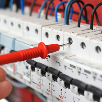 Hand of an electrician with multimeter probe at an electrical switchgear cabinet